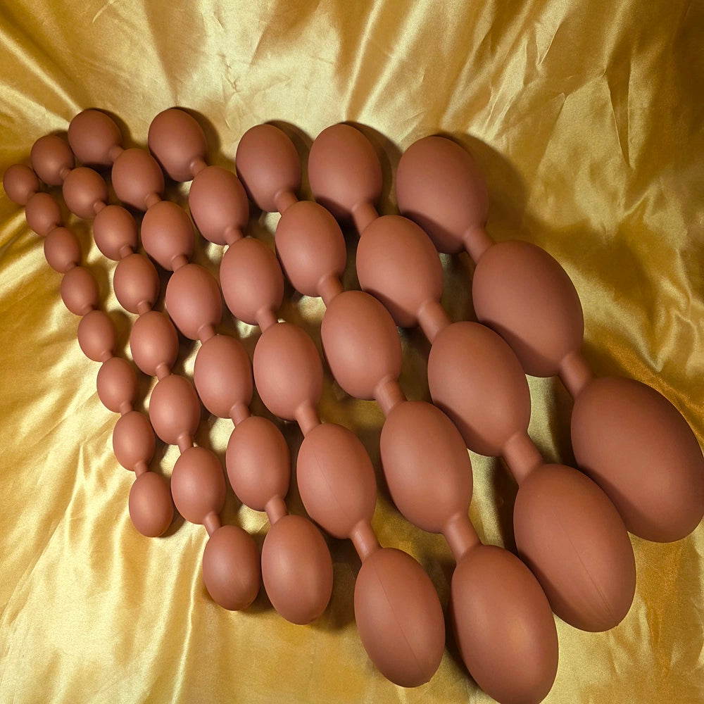 Gruppbild som visar alla storlekar av äggformade analkulor XXL i hudfärgad färg – från Small till 4XL – på guld bakgrund. Från Chambers of Love