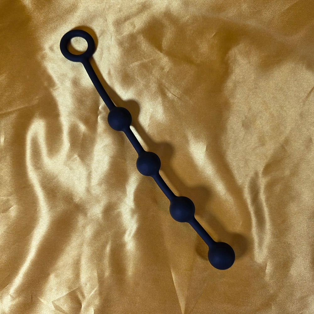 Fyra Kulors Anal Beads i liten storlek med fyra stegrande silikonkulor och säkerhetsring i änden, fotograferade på guldsidenbakgrund. Från Chambers of Love.