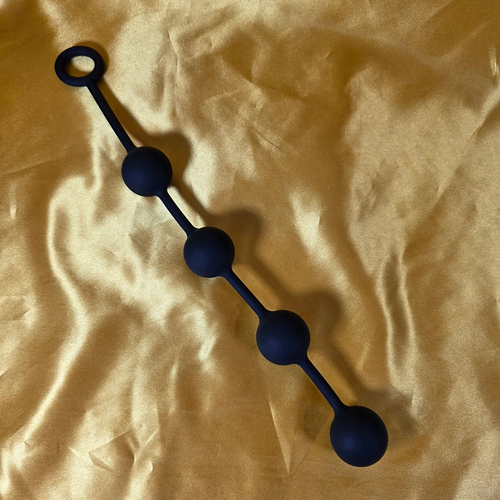 Fyra Kulors Anal Beads i mellanstorlek med fyra stegrande silikonkulor och säkerhetsring i änden, fotograferade på guldsidenbakgrund. Från Chambers of Love.