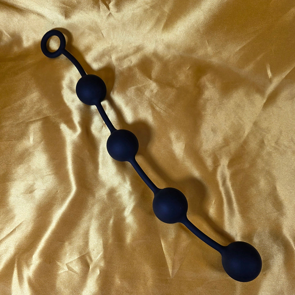 Fyra Kulors Anal Beads i stor storlek med fyra stegrande silikonkulor och säkerhetsring i änden, fotograferade på guldsidenbakgrund. Från Chambers of Love.