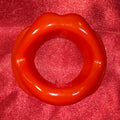 Öppen Mun Gag i rött silikon, framifrån på röd glitterbakgrund. O-ring gag för BDSM och kinky lek från Chambers of Love.