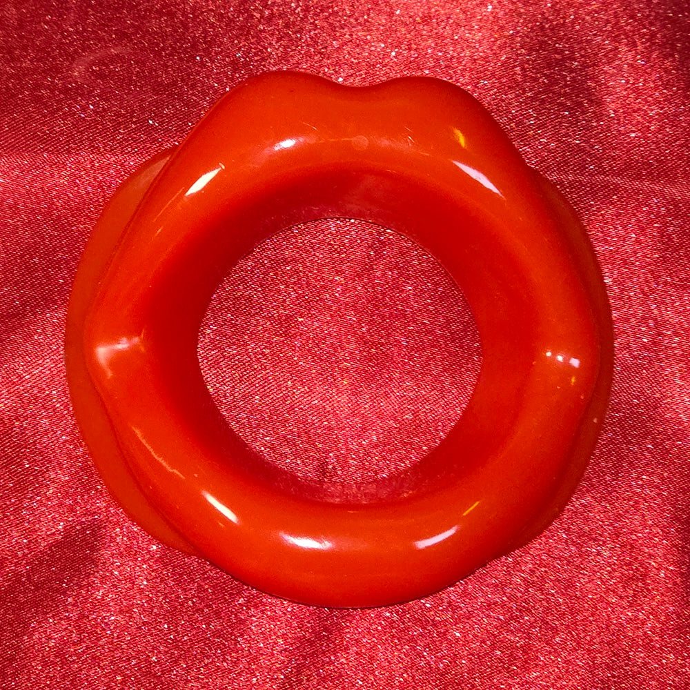 Öppen Mun Gag i rött silikon, framifrån på röd glitterbakgrund. O-ring gag för BDSM och kinky lek från Chambers of Love.