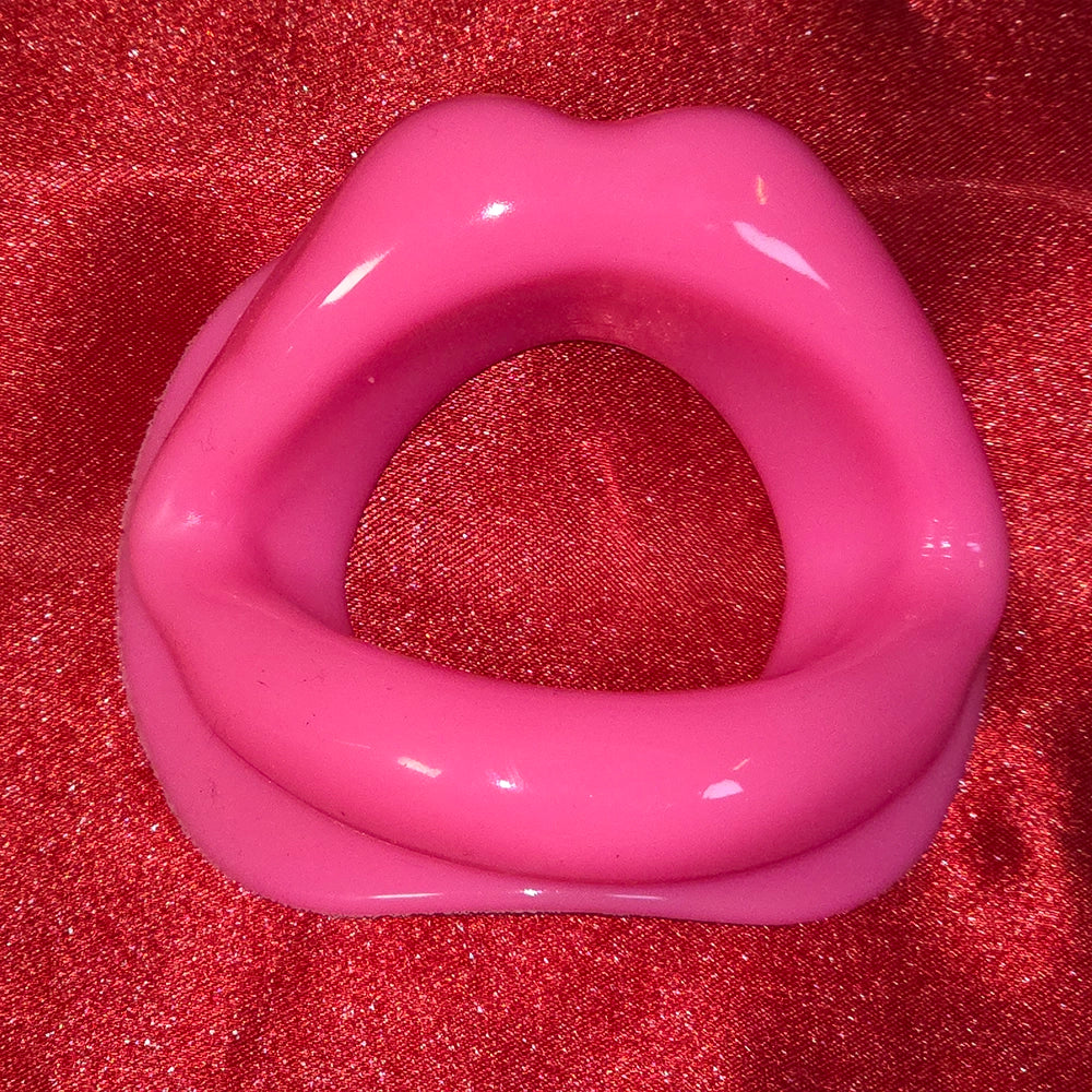 Öppen Mun Gag i rosa silikon, framifrån på röd glitterbakgrund. O-ring gag för BDSM och kinky lek från Chambers of Love.