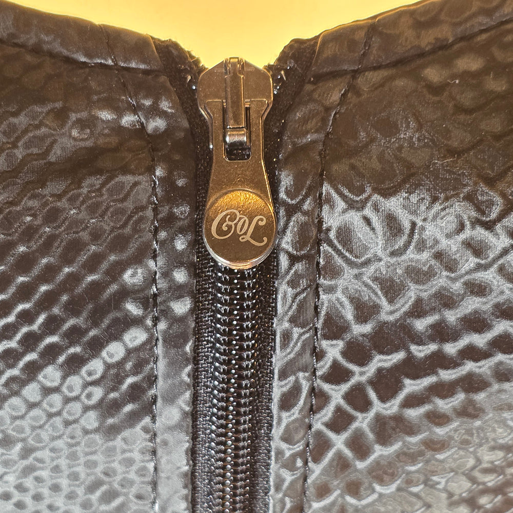 Närbild på  CoL logga dragkedja fram på svart ormskinnstopp med ormmönstrad textur från Chambers of Love